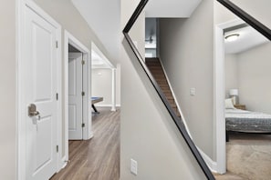 A hallway with white doors, a staircase, and a bedroom with a bed and nightstand.