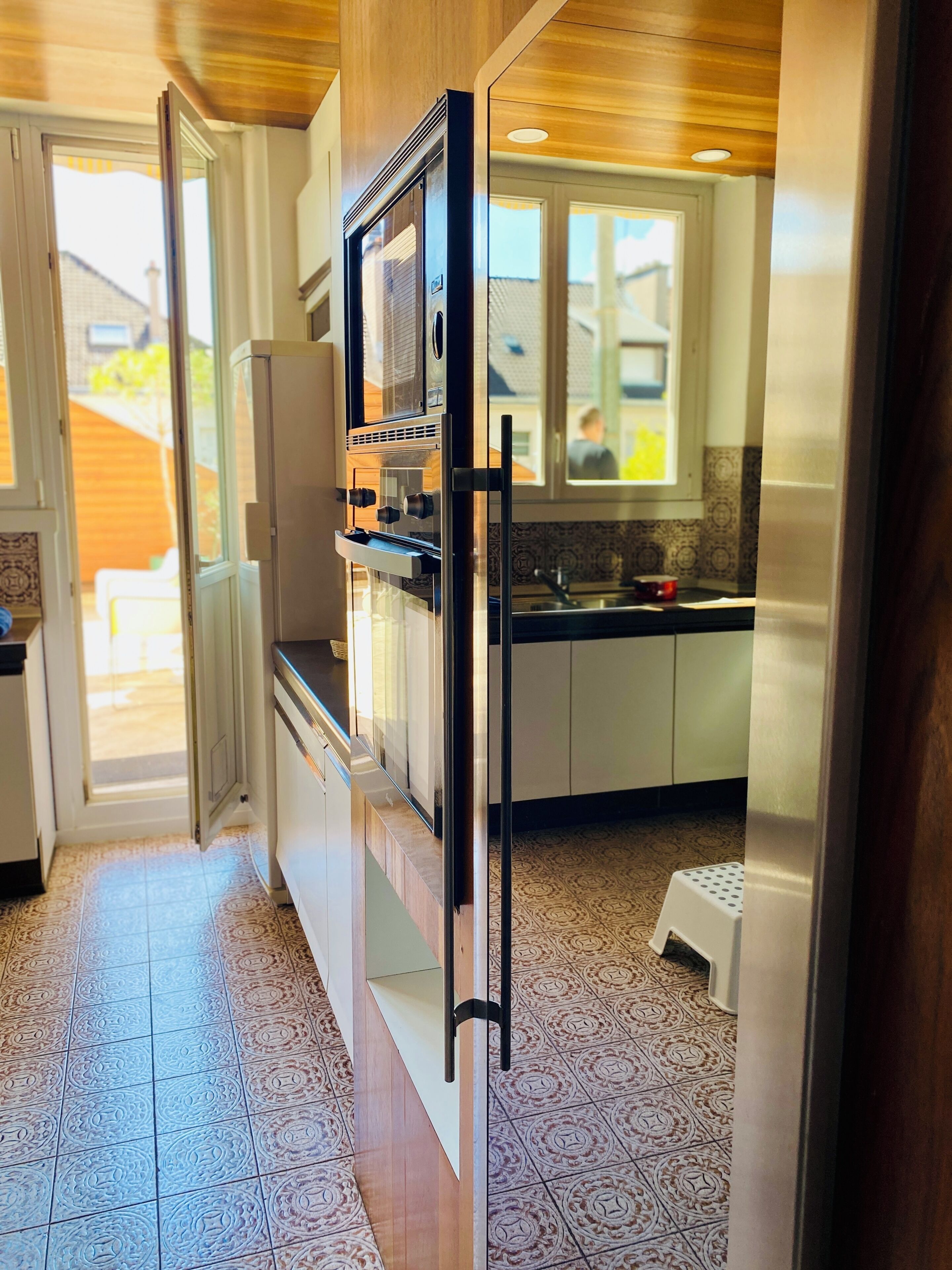 Une cuisine moderne équipée d’un four encastré, d’un réfrigérateur et d’une fenêtre donnant sur le jardin.