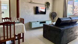 A modern living room with a dining area, a flat-screen TV mounted on the wall, a sofa, and a dining table set with chairs. - 201 | Apt. 287 • Budget-Friendly for Up to 5 Guests Near the Beach (Bombinhas)