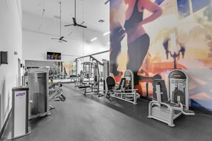 A gym with various exercise machines, a large mirror, and a wall-mounted TV.