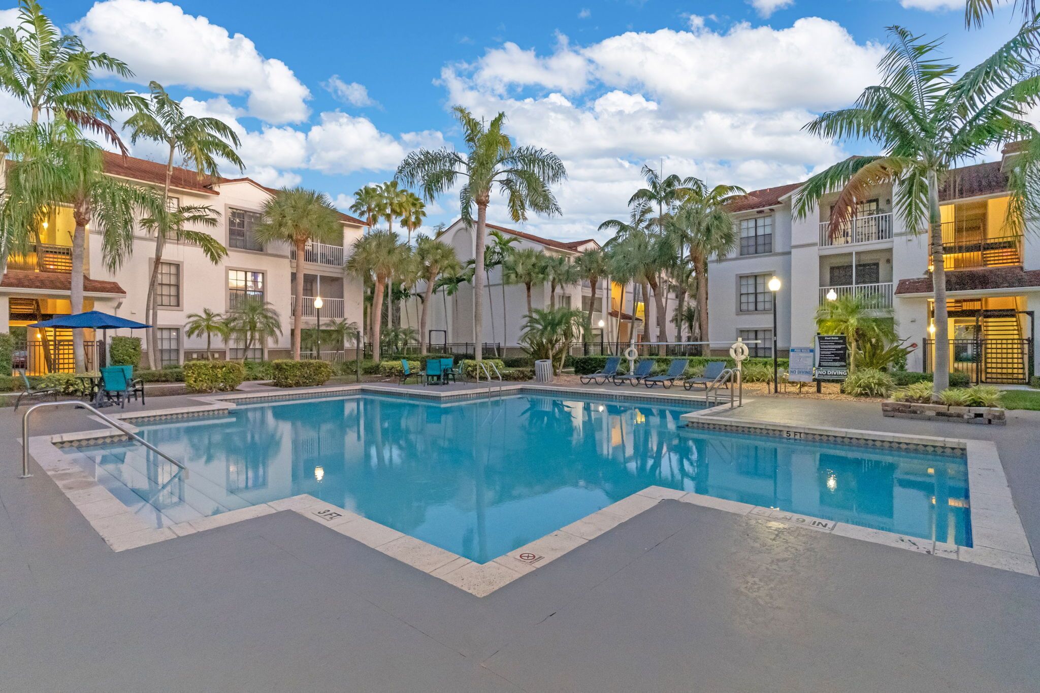 A swimming pool surrounded by palm trees and a building with balconies.
