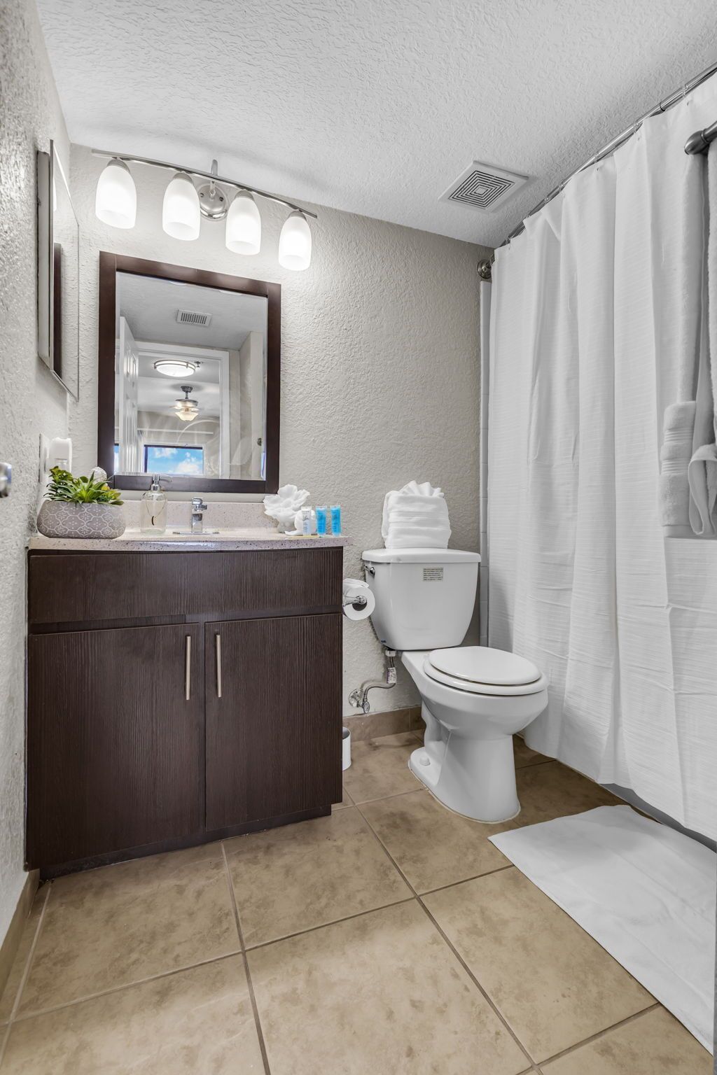 A bathroom with a dark wood vanity, white toilet, and a shower curtain.