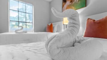 A bed with a white swan-shaped towel, a window with a view, and a painting on the wall.