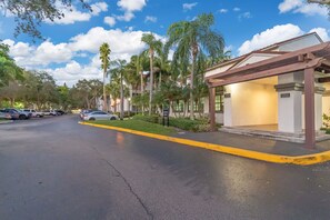 A hotel entrance with a covered waiting area, palm trees, and a parking lot.