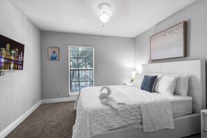 A bedroom with a bed, a window with blinds, a wall-mounted artwork, and a ceiling light.