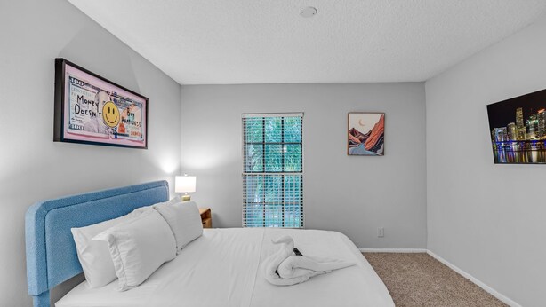 A hotel room with a bed, a window with blinds, a wall-mounted artwork, and a cityscape painting. - Port Royale Apartments (Fort Lauderdale)