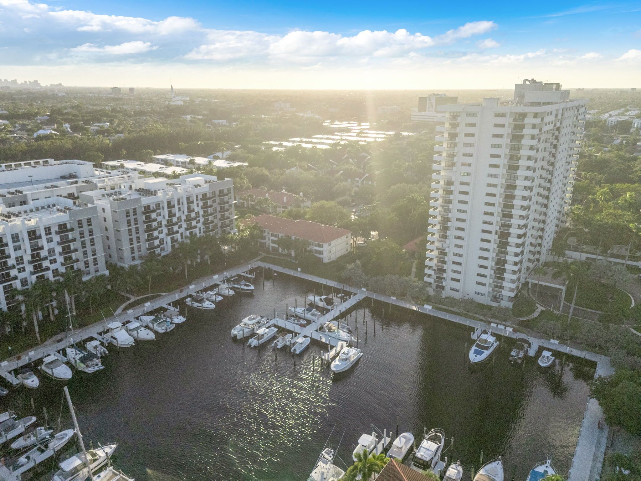 An aerial view of a marina with boats docked, surrounded by residential buildings and a large white high-rise building.