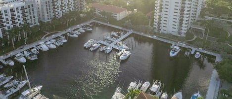 Une vue aérienne d’une marina où sont amarrés des bateaux, entourée d’immeubles résidentiels et d’un grand immeuble blanc de grande hauteur.