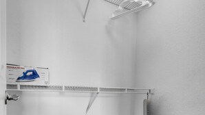 Een kleine inbouwkast met witte wanden, een metalen plank, een doos op de vloer en een plafondlamp.