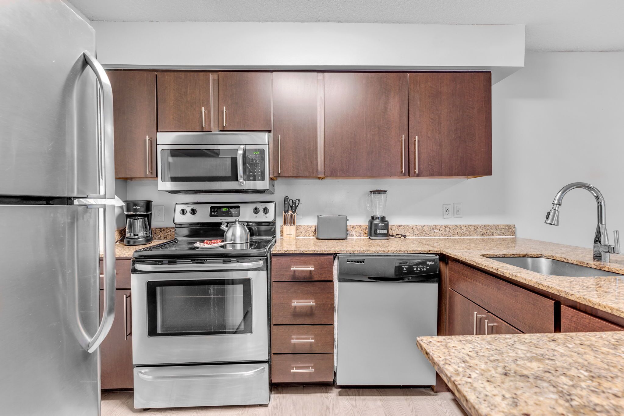A modern kitchen with stainless steel appliances, wooden cabinets, granite countertops, and a built-in dishwasher.