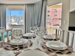 A dining table set with plates, glasses, and cutlery, with a view of buildings through a window. - 103 | Res. 287 • Affordable for up to 7 People, Close to the Beach (Bombinhas)
