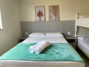 A hotel room with a bed, a green blanket, two rolled towels, and two framed pictures on the wall. - 287.203 - AP Aurora: Affordable, cozy and just steps from the beach (Bombinhas)
