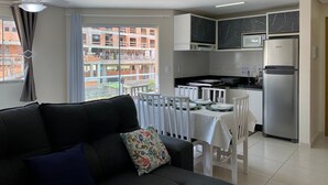 A modern apartment with a dining area, kitchenette, and a balcony with a view of a building under construction. - 287.203 - AP Aurora: Affordable, cozy and just steps from the beach (Bombinhas)