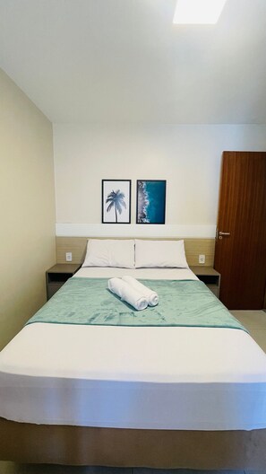 Ein Hotelzimmer mit einem Bett, zwei gerahmten Bildern an der Wand, einer Holztür und einem Nachttisch.