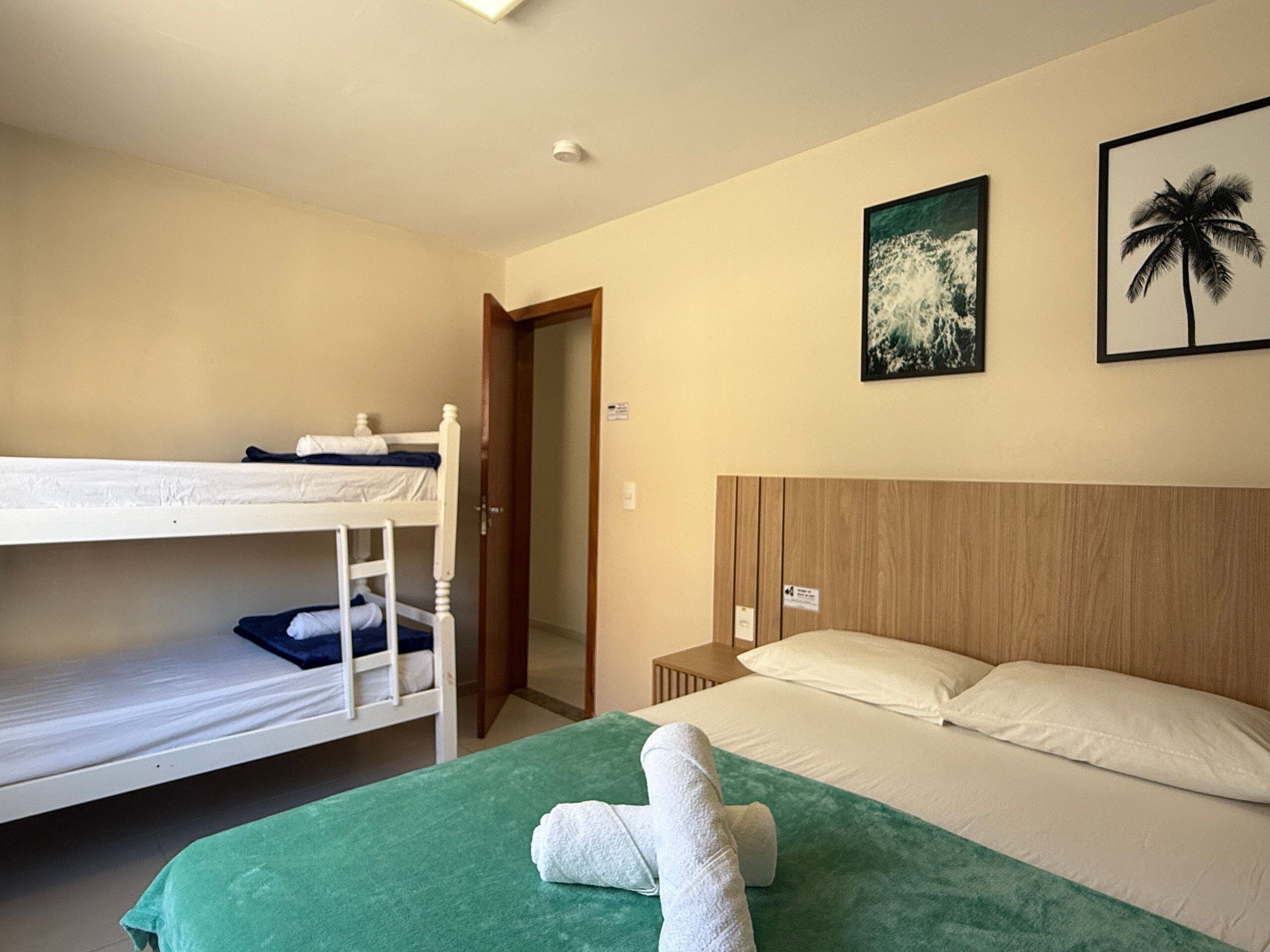Een kamer met een stapelbed, een enkel bed met een groene deken, en twee fotolijstjes aan de muur.