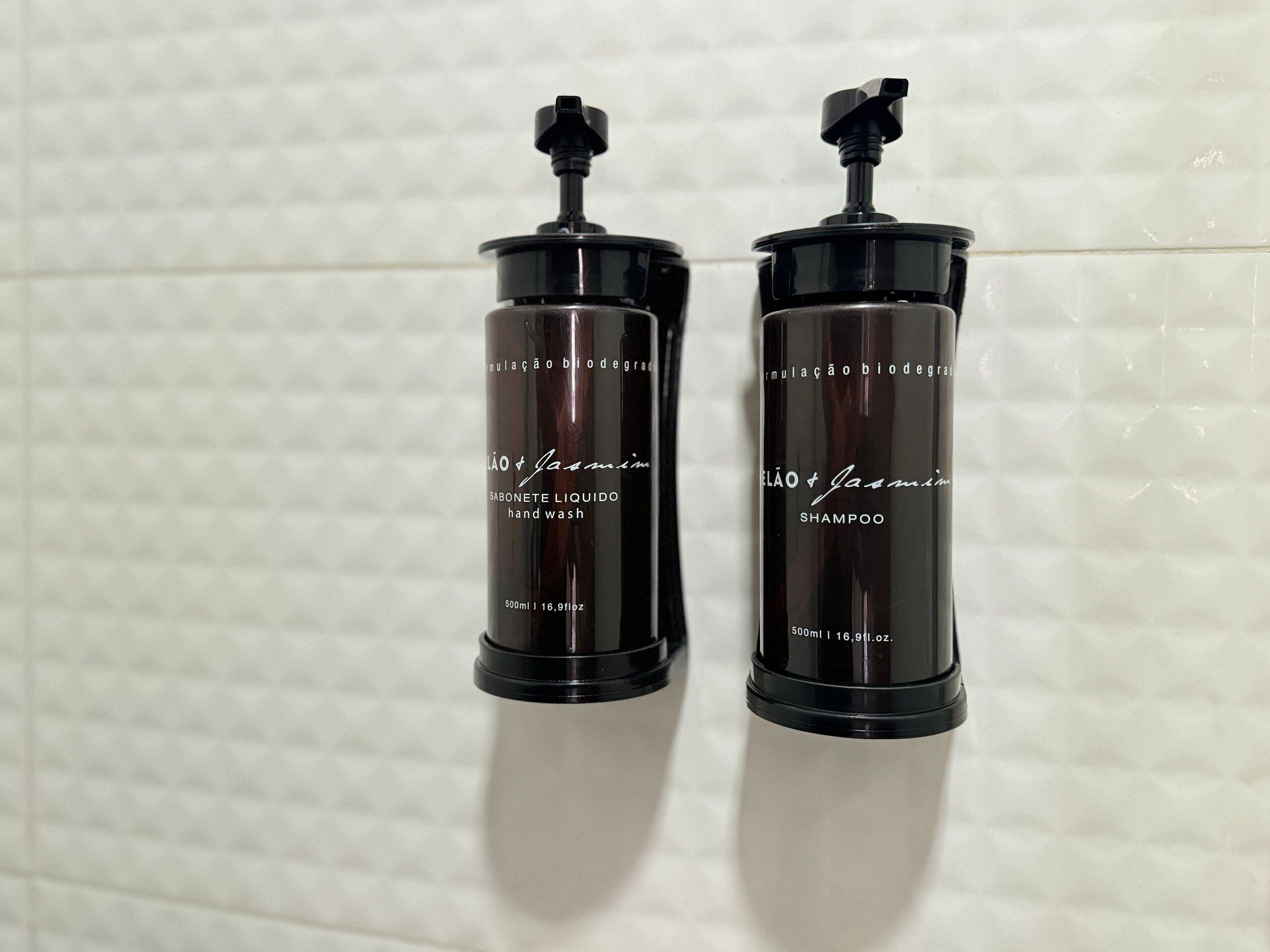 To sorte flasker med håndvask og shampoo, placeret op ad en flisevæg.