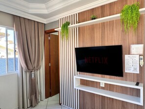Uma sala de estar moderna com uma TV de tela plana fixada numa parede de madeira, uma porta deslizante e uma janela com cortinas.