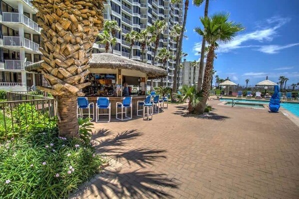 A hotel with a bar area, outdoor seating, a pool, and palm trees. - NEW! Beachfront 2BR 11th Floor Views, Saida Royale SPI (South Padre Island)