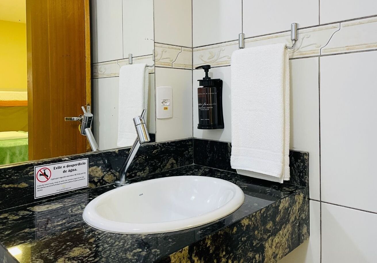 A bathroom with a white sink, black marble countertop, and a mirror. There is a towel hanging on the wall and a soap dispenser.