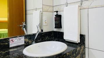 A bathroom with a white sink, black marble countertop, and a mirror. There is a towel hanging on the wall and a soap dispenser.