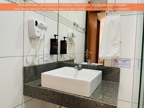 Un bagno d'hotel con un lavandino bianco, un asciugacapelli e due flaconi di shampoo.