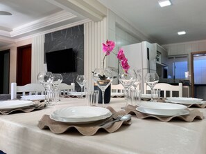 A dining table set with plates, glasses, and a vase with pink flowers. - 01 | Res. 364 • Ground floor - 3 bedrooms - 5min walk to the Sea (Bombinhas)