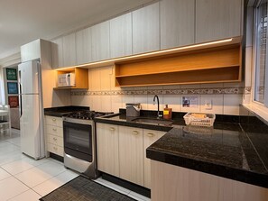 A modern kitchen with wooden cabinets, a built-in oven, a gas stove, and a black countertop. - 01 | Res. 364 • Ground floor - 3 bedrooms - 5min walk to the Sea (Bombinhas)