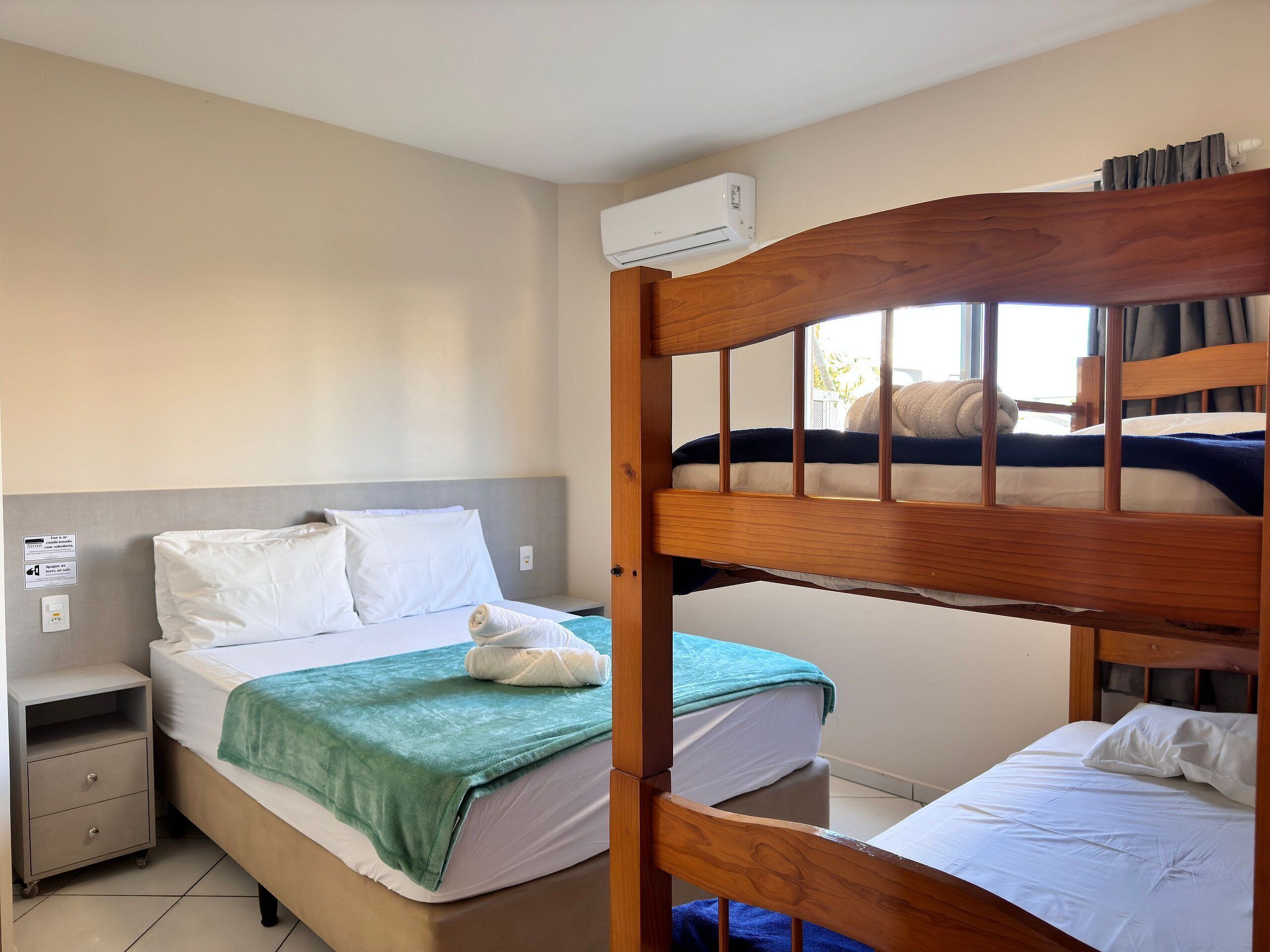 A bunk bed room with a wooden headboard, a nightstand, a green blanket, and a white pillow.