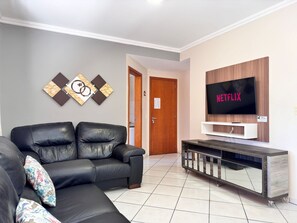Ein modernes Wohnzimmer mit einer schwarzen Ledersofa, einem flachbildfernseher an einer Holzwand und einer schlichten Unterhaltungsanlage.