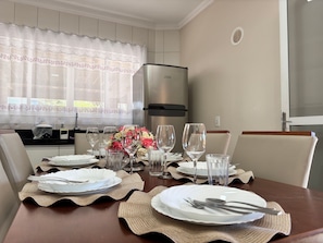 A dining table set with plates, cutlery, and glasses, with a bouquet of flowers in the center. - 03 | Apt. 364 • Apt. with Balcony - 2 Bedrooms - 5 min Walk to the Sea (Bombinhas)