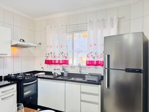 A modern kitchen with white cabinets, a stainless steel refrigerator, a gas stove, and a window with floral curtains. - 04 | Apt. 364 • No Balcony | Great Value for Money | Prime Location (Bombinhas)