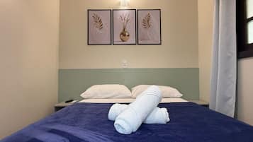 Quarto de hotel com cama, almofadas, mesa de cabeceira e luminária fixa na parede.