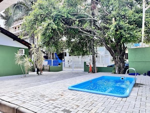 Ein Swimmingpool mit blauer Innenauskleidung, umgeben von einer gepflasterten Fläche mit Bäumen und einem weißen Zaun.