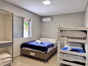 Ein Schlafzimmer mit Etagenbett, einem Einzelbett, einem Fenster mit Jalousien, einer Klimaanlage und einem Kleiderschrank.