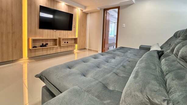 Een moderne slaapkamer met een groot bed, een flatscreen televisie bevestigd aan een houten muur, en een deur die naar een andere kamer leidt.