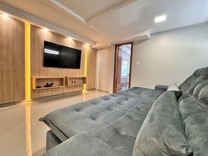 Ein modernes Schlafzimmer mit einem großen Bett, einem Flachbildfernseher an einer Holzwand und einer Tür zu einem weiteren Raum.