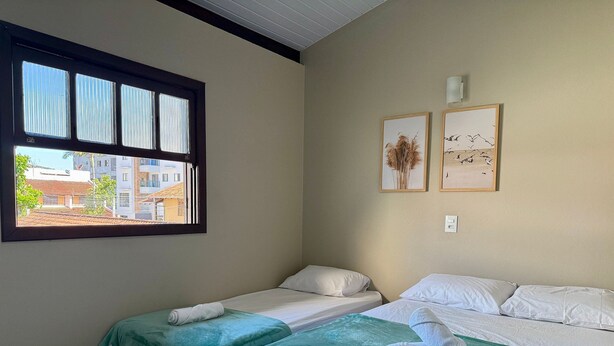 Habitación de hotel con dos camas, una ventana con persianas y dos cuadros enmarcados en la pared.