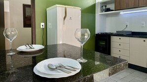 Una cocina moderna con encimera de mármol, un refrigerador blanco y una zona de comedor con un plato, cubiertos y dos copas de vino.