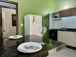 Een moderne keuken met een marmeren aanrecht, een witte koelkast, en een eethoek met een bord, bestek en twee wijnglazen.