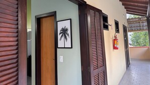 Un pasillo con una puerta de madera, un cuadro con una palmera y un extintor en la pared.