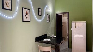 Un área de comedor con una mesa preparada para dos personas, una obra de arte enmarcada en la pared y un refrigerador en la esquina.