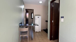 A small kitchen area with a refrigerator, a table, and a chair. - 02 | Res. 305 • Cozy Apartment for Couple – 5min from the Beach (Bombinhas)