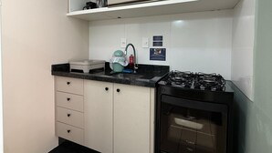 A compact kitchen with a gas stove, a sink, and a microwave. There are cabinets with drawers and a countertop. - 02 | Res. 305 • Cozy Apartment for Couple – 5min from the Beach (Bombinhas)