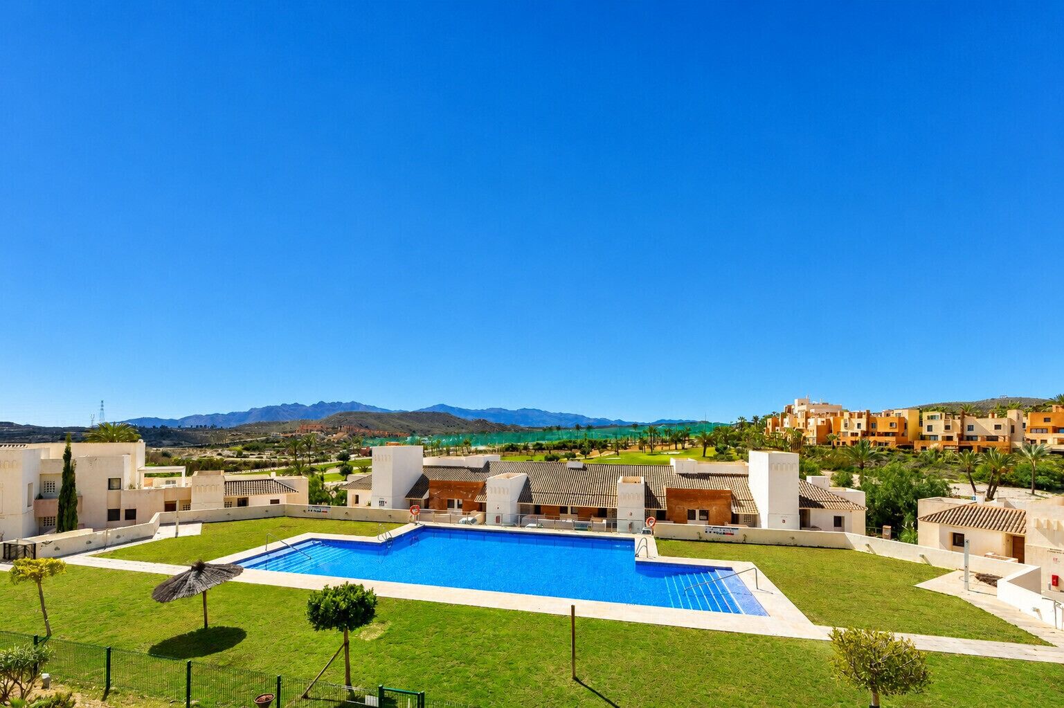 A swimming pool with a view of mountains, surrounded by buildings and greenery.