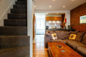 Eine Treppe führt zu einer Küche mit einer Holztischplatte und einem Sofa mit gemusterten Kissen.