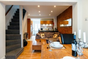 Ein modernes Interieur mit einer Treppe, einem Essbereich mit Tisch für zwei Personen und einer Küche im Hintergrund.