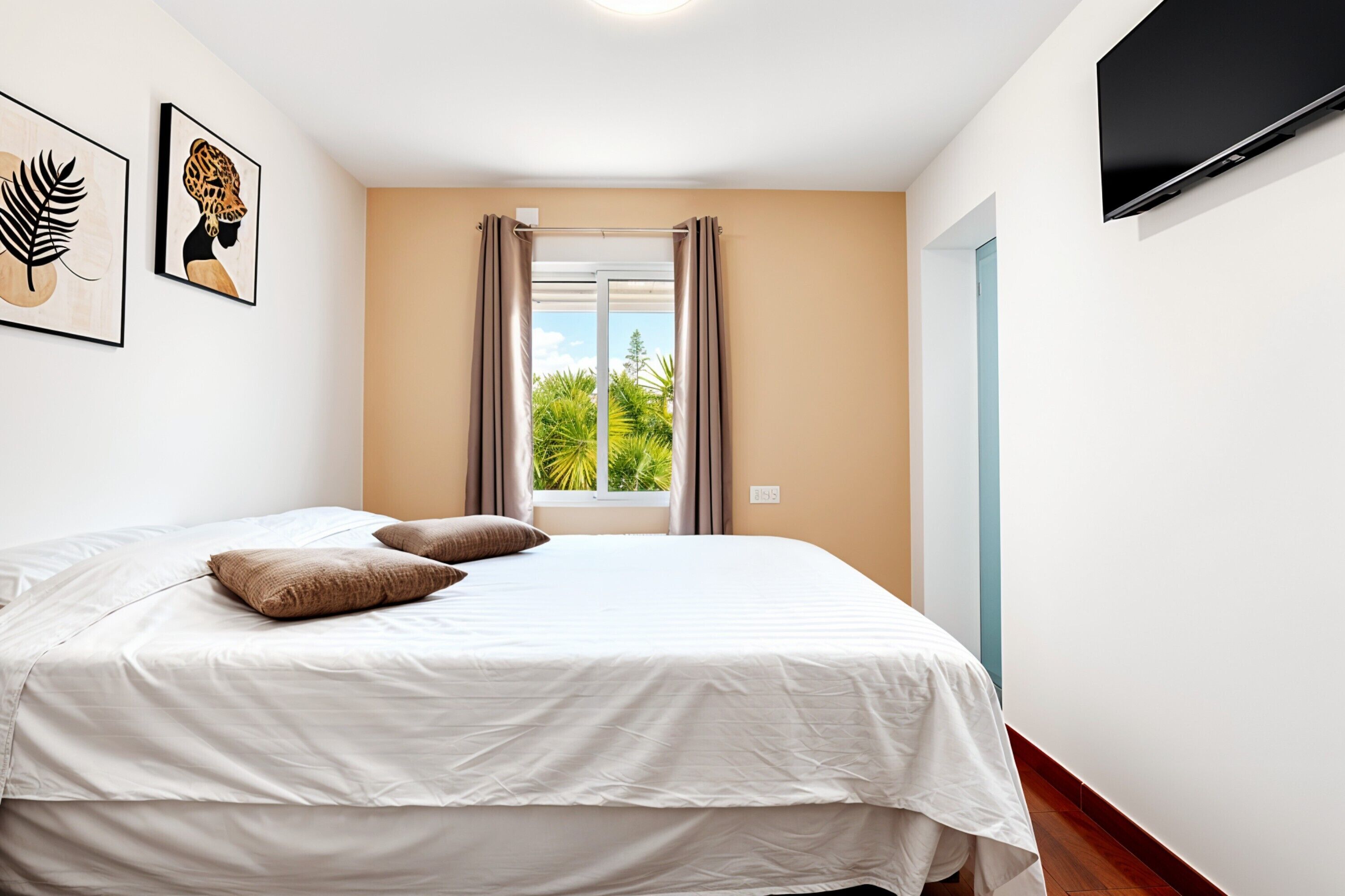 Une chambre à coucher avec un lit, une fenêtre avec des rideaux, un téléviseur à écran plat et des œuvres d’art accrochées au mur.