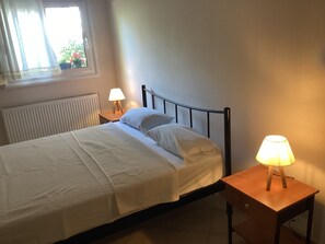Ein Einzelbett mit weißem Bettbezug, zwei Nachttische mit Lampen, ein Fenster mit Vorhängen und eine Heizung.