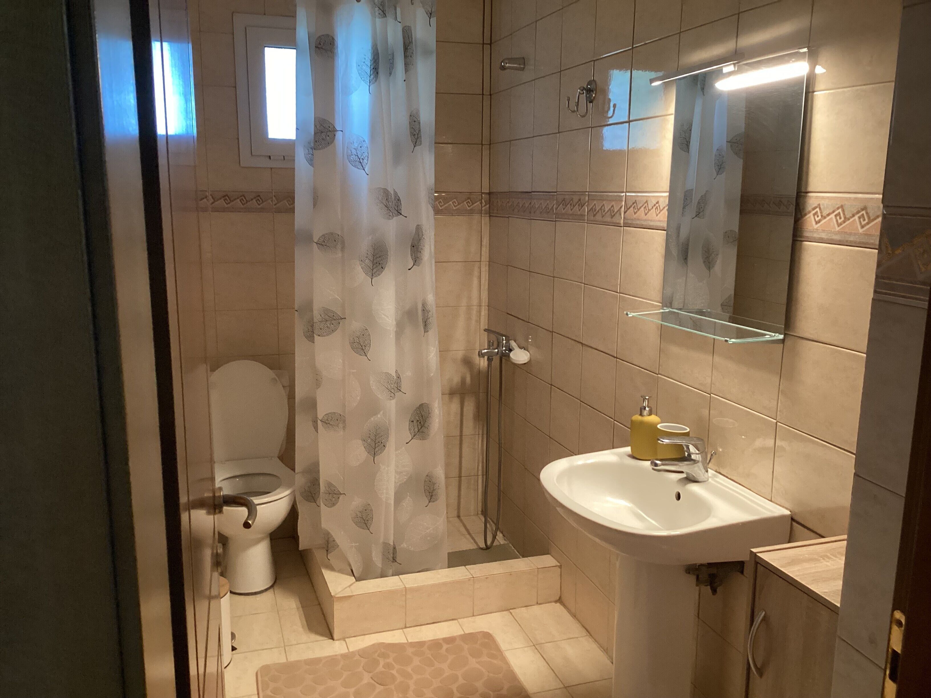 A bathroom with a toilet, shower, sink, and a mirror.