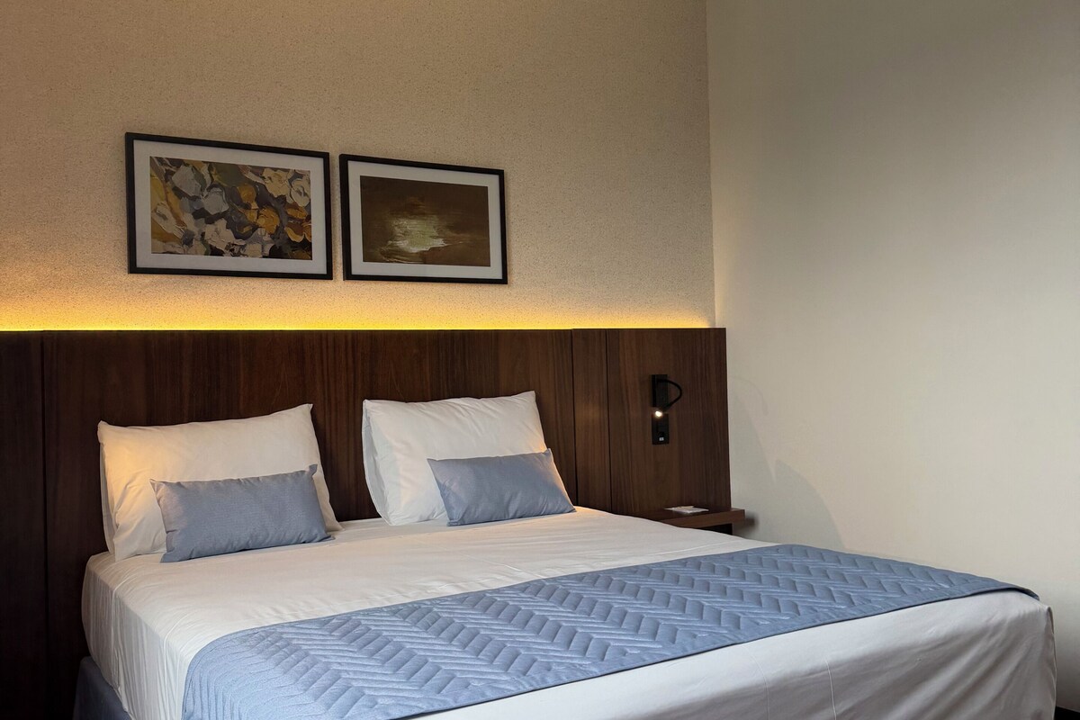 A hotel room with a bed, a nightstand, and two framed pictures on the wall.